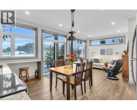A dining room with a wooden table and chairs, a couch, and a view of the outdoors through large windows.