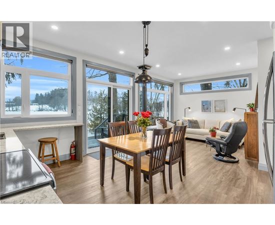 A dining room with a wooden table and chairs, a couch, and a view of the outdoors through large windows.