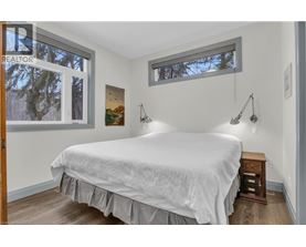 A bedroom with a bed, nightstand, and two windows.