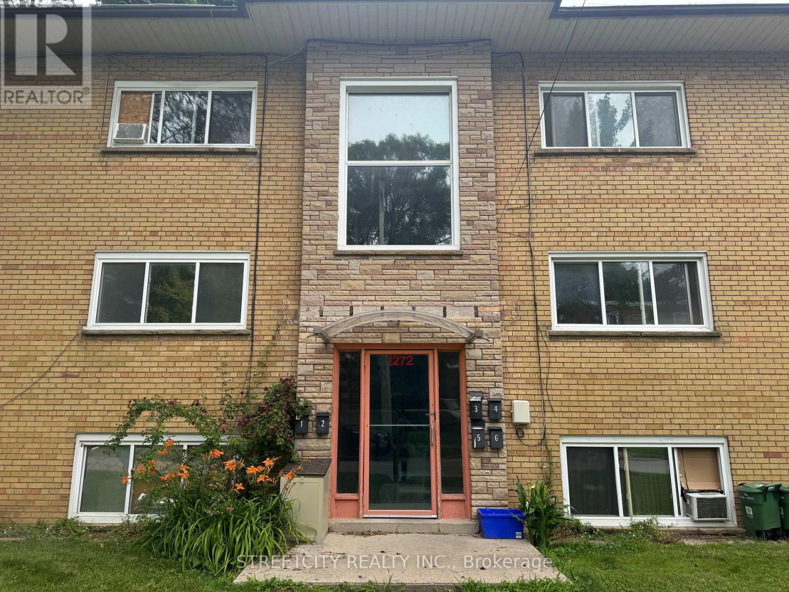 A brick building with a red door and windows on the second floor.