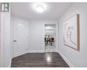 A room with a white door, a dining table with chairs, a painting on the wall, and a wooden floor.