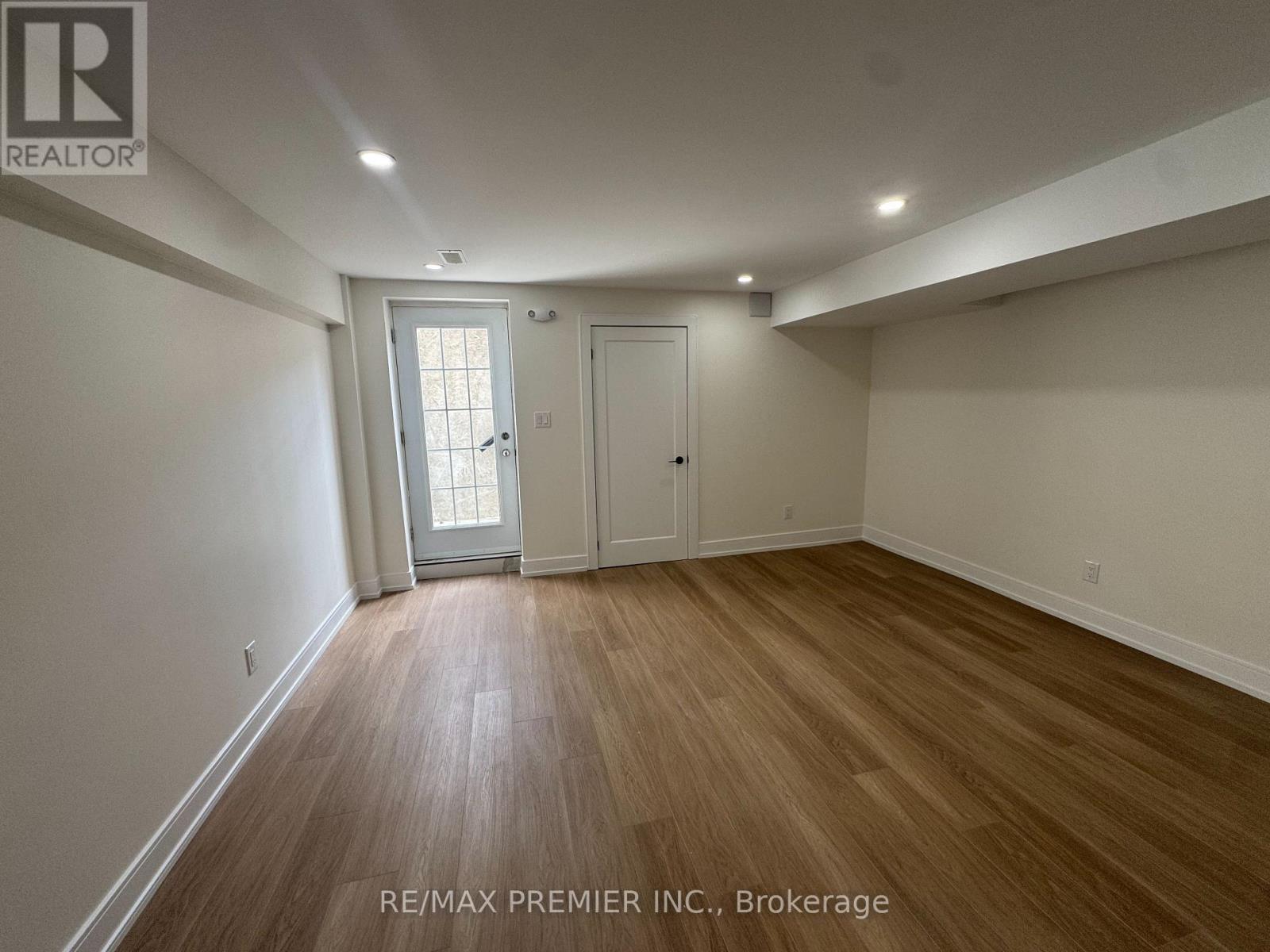 A room with wooden flooring and white walls, with a door and a window.