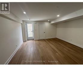 A room with wooden flooring and white walls, with a door and a window.