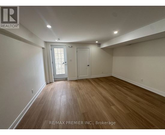 A room with wooden flooring and white walls, with a door and a window.