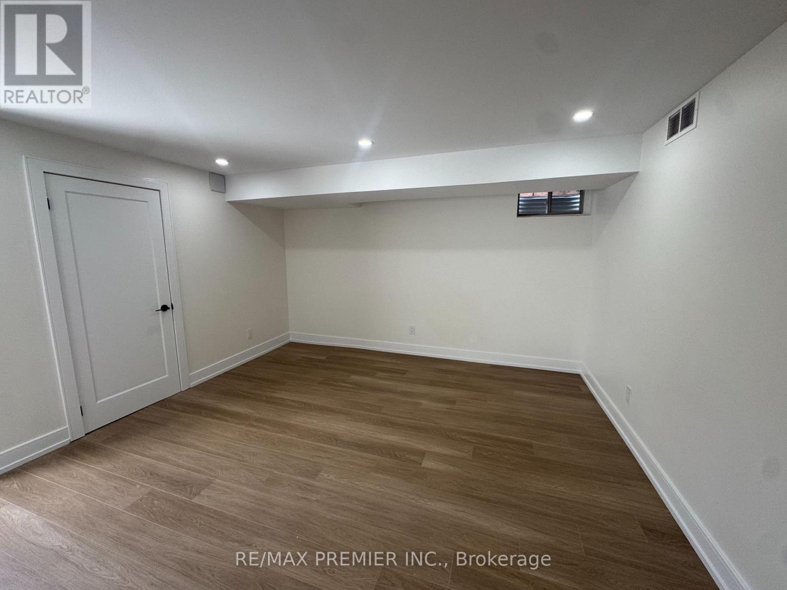 A room with wooden flooring and white walls, with a door on the left and a small window on the right.