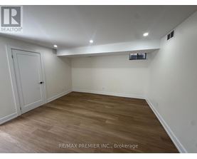 A room with wooden flooring and white walls, with a door on the left and a small window on the right.