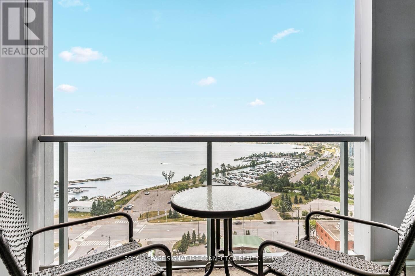 A balcony with a table and chairs overlooking a parking lot and a body of water.