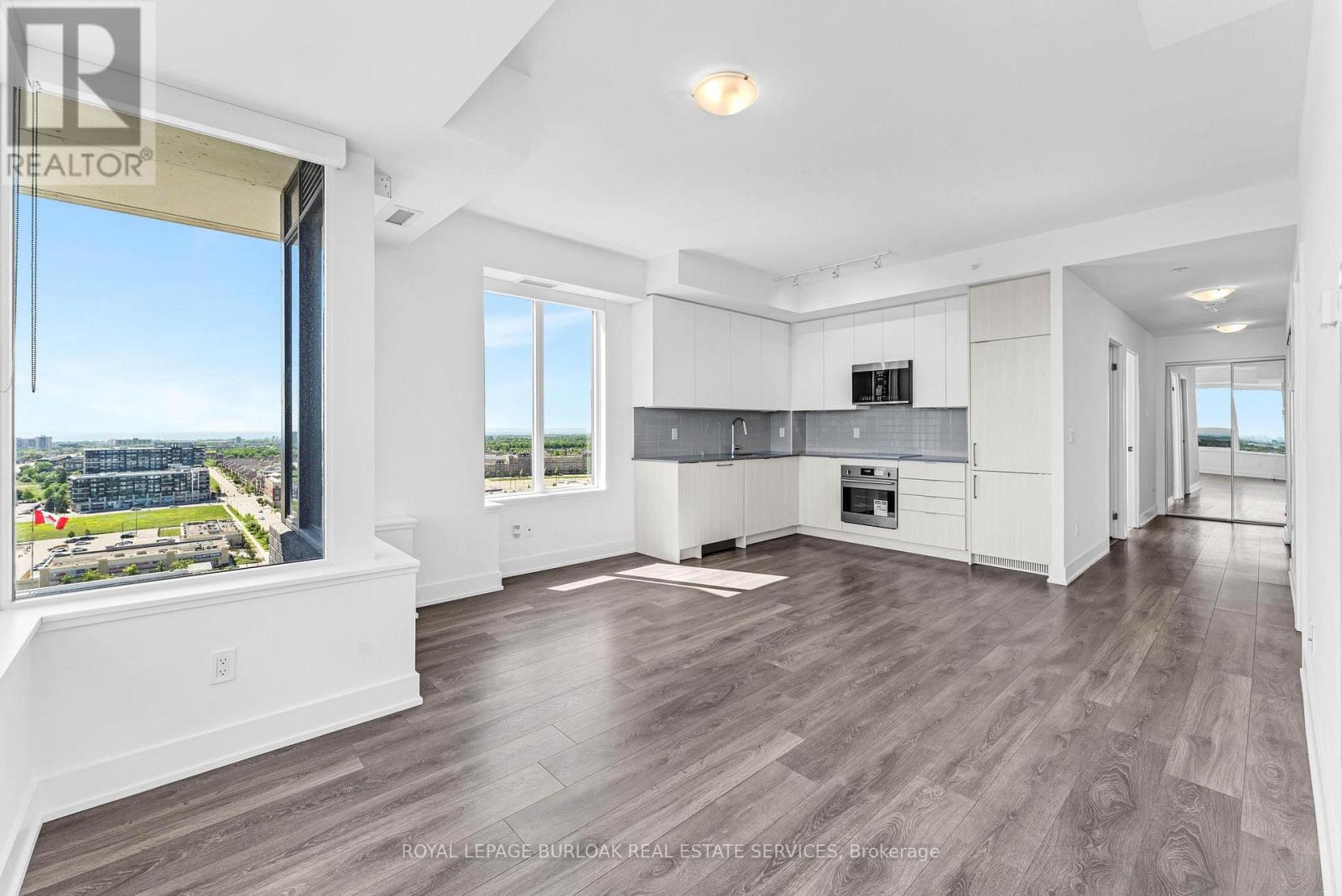 A spacious, well-lit living room with a large window overlooking a cityscape.