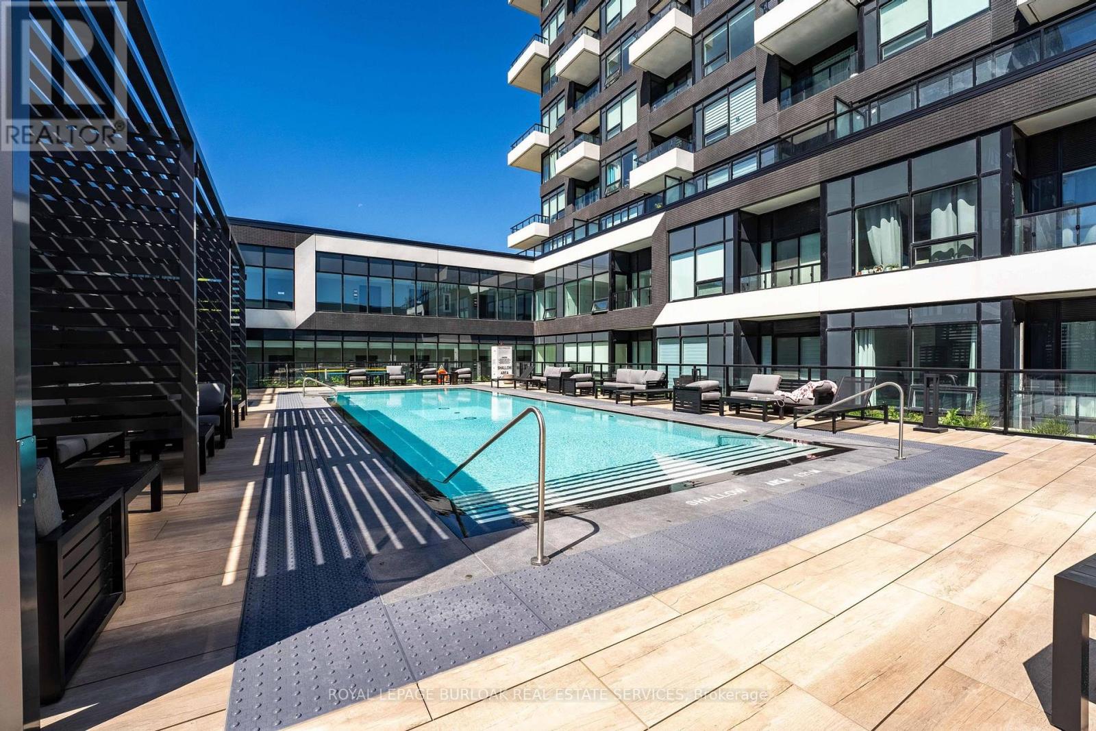 A pool area with a wooden deck and a building in the background.
