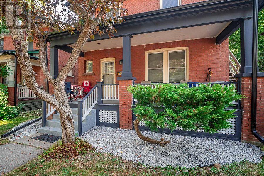 A red brick house with a porch and a tree in front.