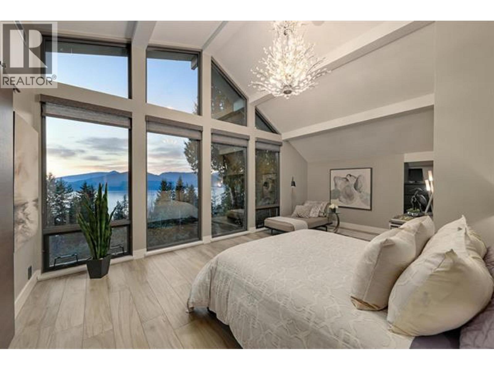 A bedroom with a large bed and a view of the mountains through the windows.
