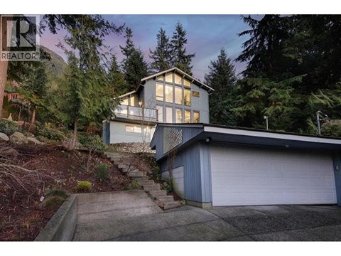 A house with a garage is surrounded by trees.