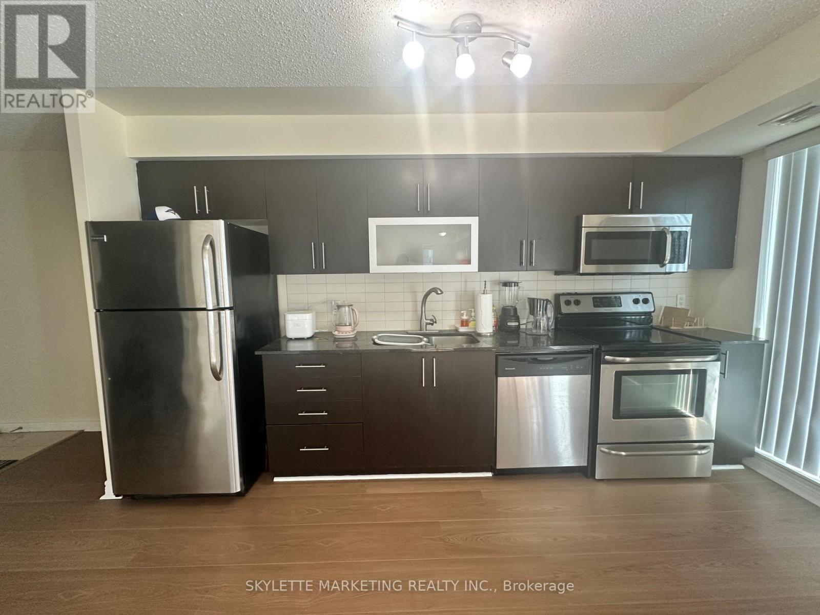 A kitchen with a refrigerator, microwave, oven, and sink.