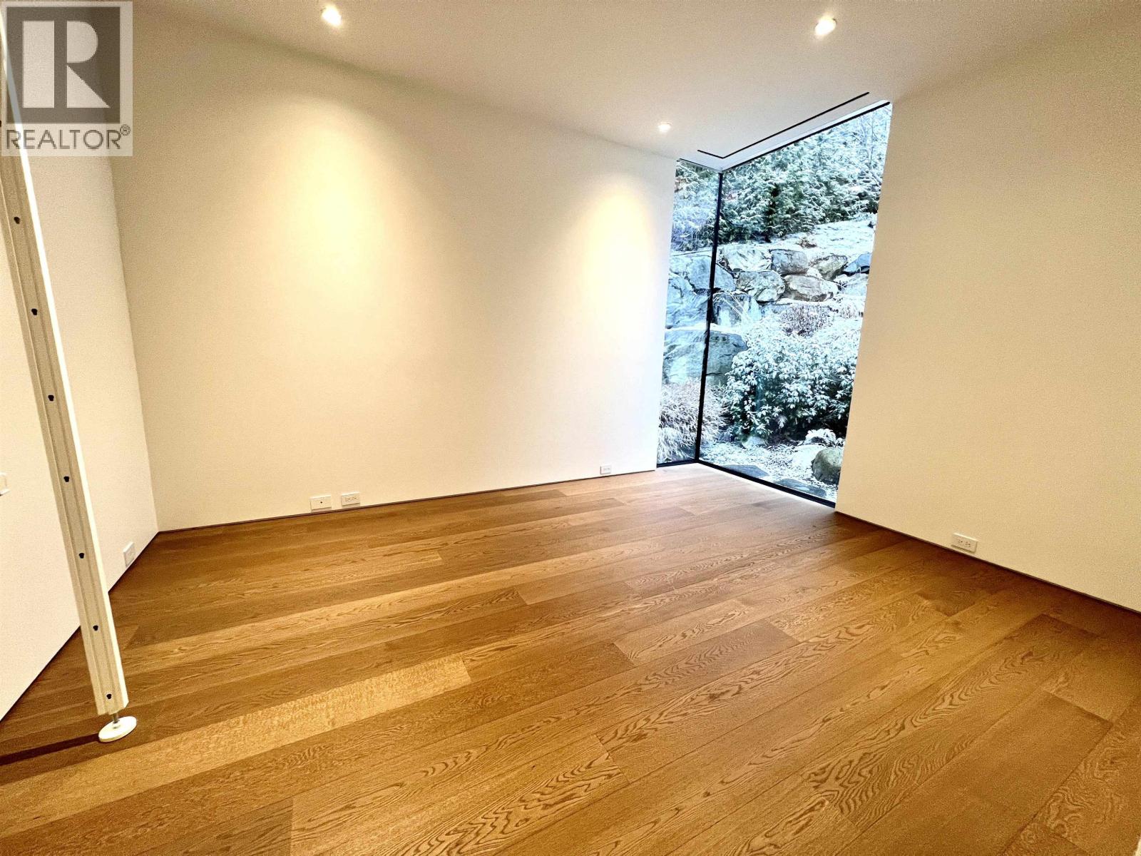 A room with wooden flooring and a window with a view of trees.