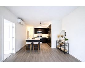 A modern kitchen with a bar stool and a small shelf with decorative items.