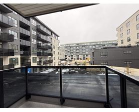 A balcony with a railing overlooks a parking lot and buildings.