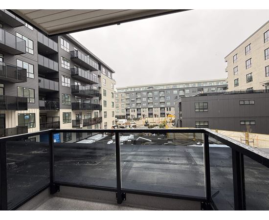 A balcony with a railing overlooks a parking lot and buildings.