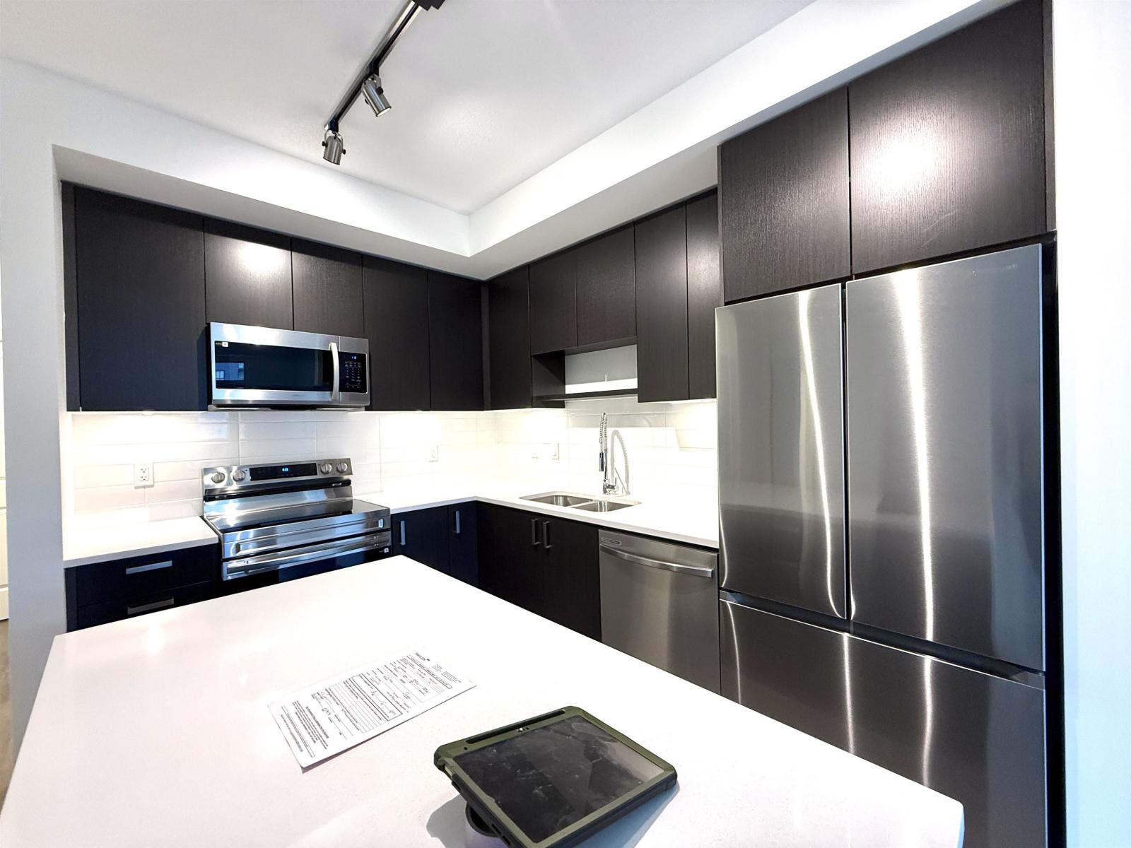 A modern kitchen with a white counter top and stainless steel appliances.
