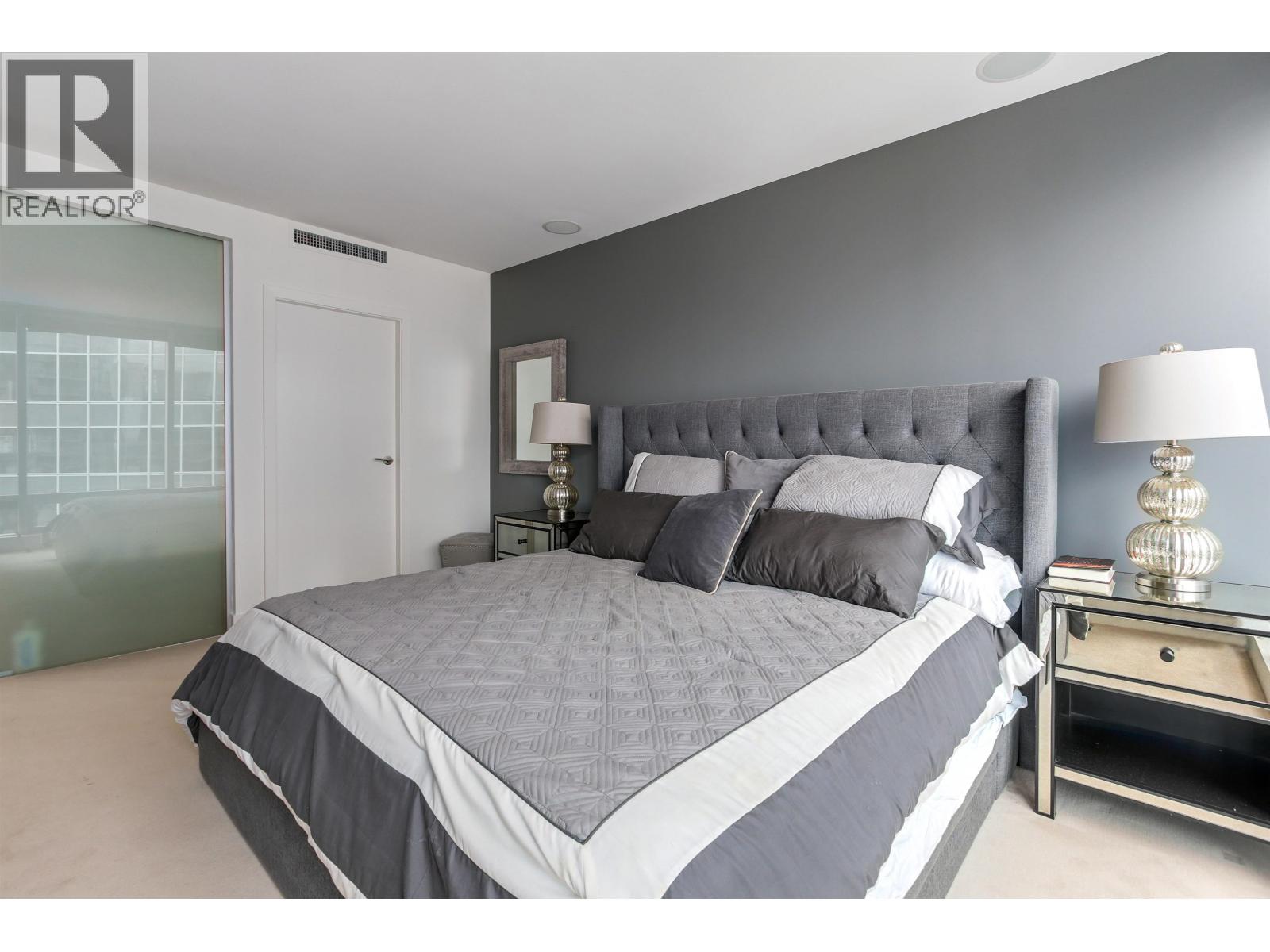 A bedroom with a large bed and a nightstand with a lamp.