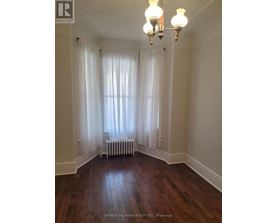 A room with a window covered by white curtains and a radiator beneath it.