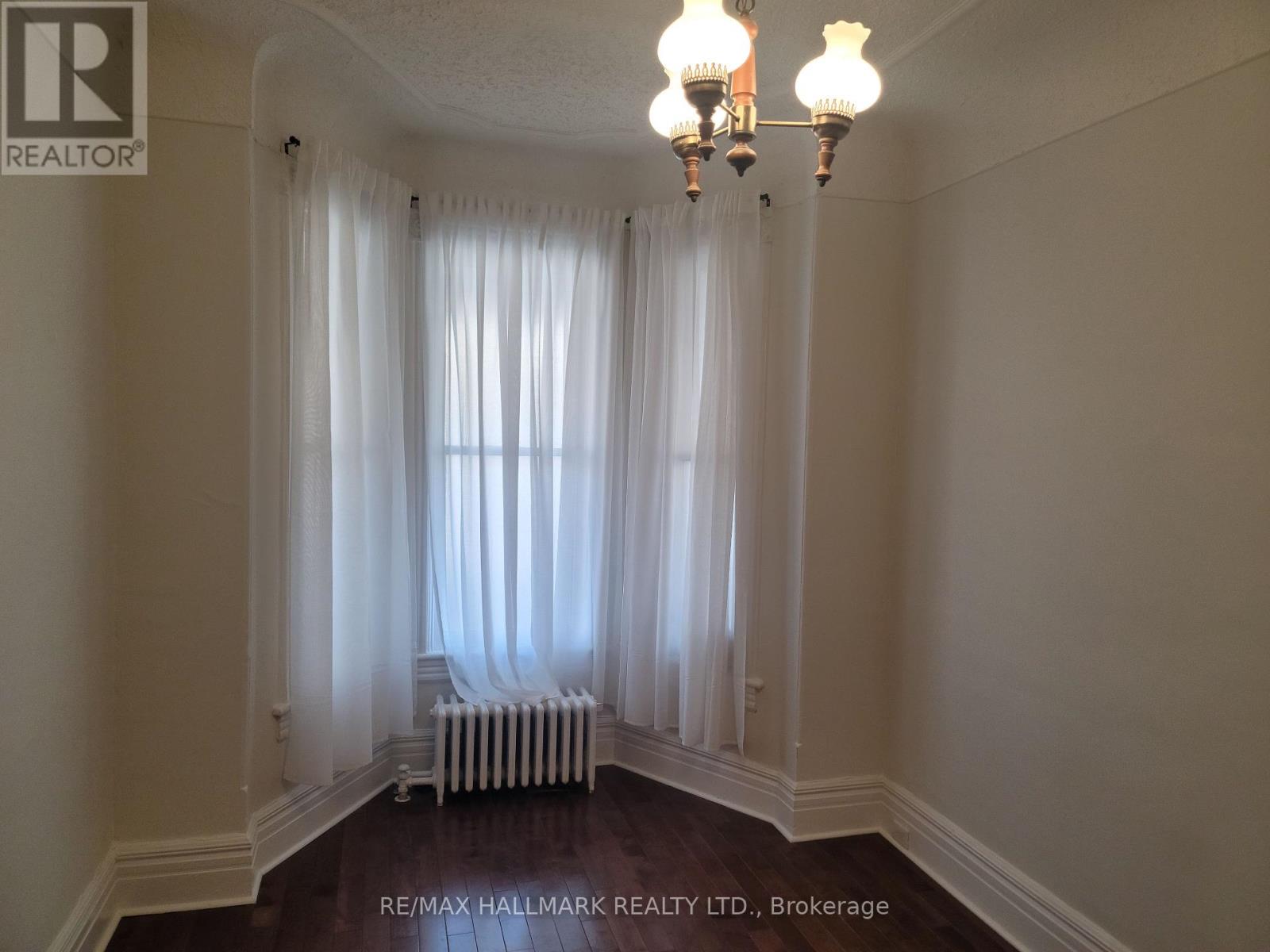 A room with a chandelier, a window with curtains, and a radiator.