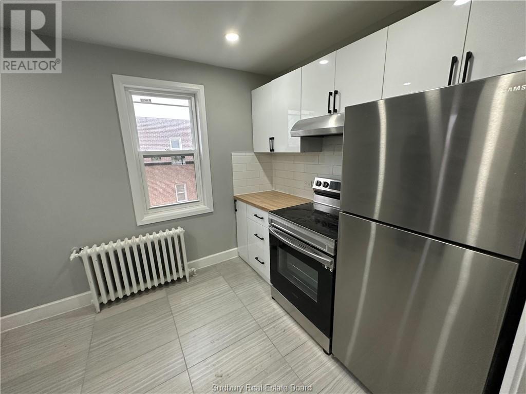 A kitchen with a stainless steel refrigerator and a window with a white frame.