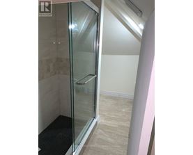 A shower area with a glass door and a black mat on the floor.