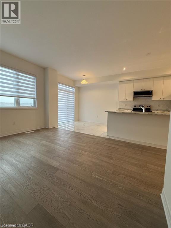 A spacious room with wooden flooring and a kitchen area with white cabinets.