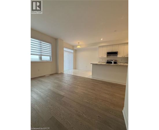 A spacious room with wooden flooring and a kitchen area with white cabinets.