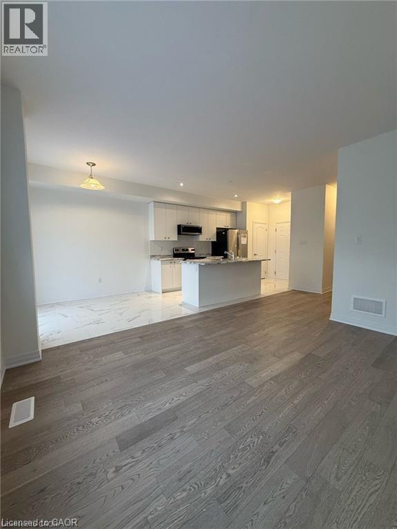 A spacious room with wooden flooring and a kitchen area in the background.