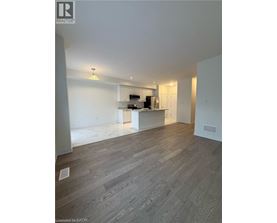 A spacious room with wooden flooring and a kitchen area in the background.