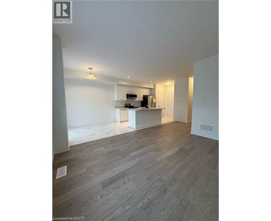 A spacious room with wooden flooring and a kitchen area in the background.