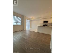A spacious room with wooden flooring and a kitchen area in the background.