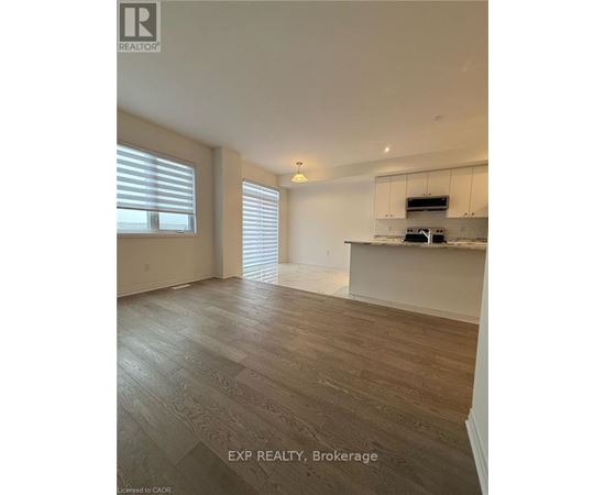 A spacious room with wooden flooring and a kitchen area in the background.