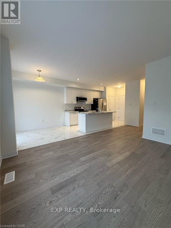 A room with wooden flooring and a kitchen area in the background.