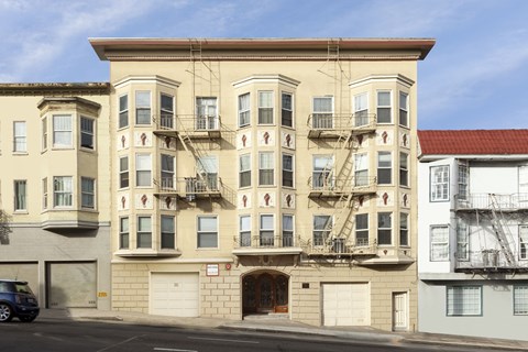 A tan building with a red roof is to the right of a tan building with a blue sky in the background.