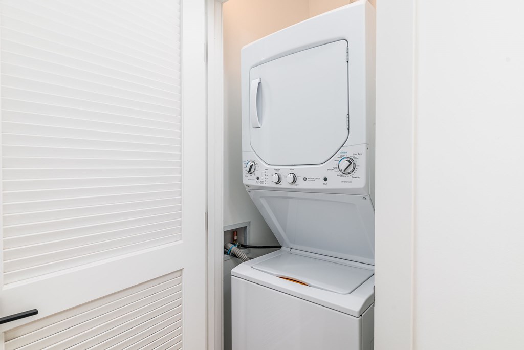 A white dryer is in a small space next to a window with blinds.