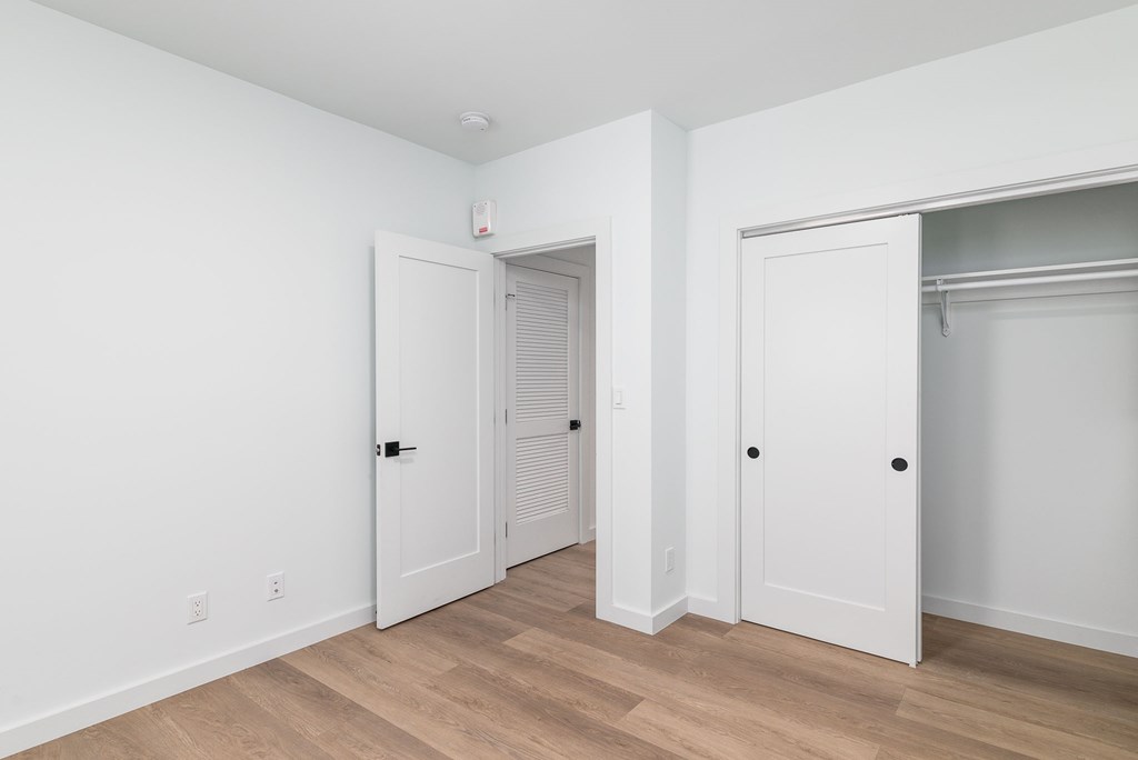 A room with white walls and wooden floors, with three doors.