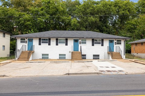 A white two-story house with a black roof and blue doors.