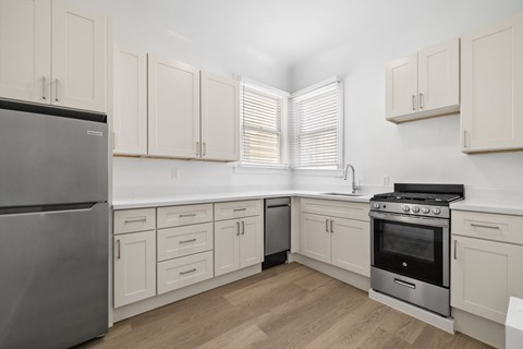 A kitchen with a stainless steel refrigerator, a stove, and white cabinets.