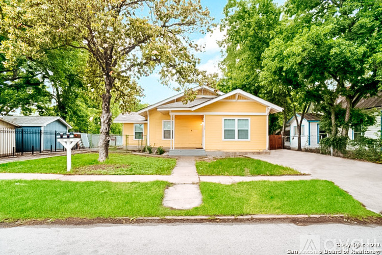 A yellow house with a white fence and green trees in the background.