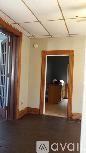 A room with a wooden floor and a white ceiling with a doorway leading to another room.