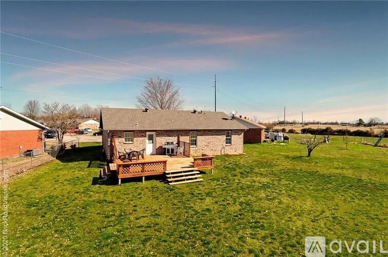 A house with a brown roof and a wooden deck is surrounded by a grassy field.
