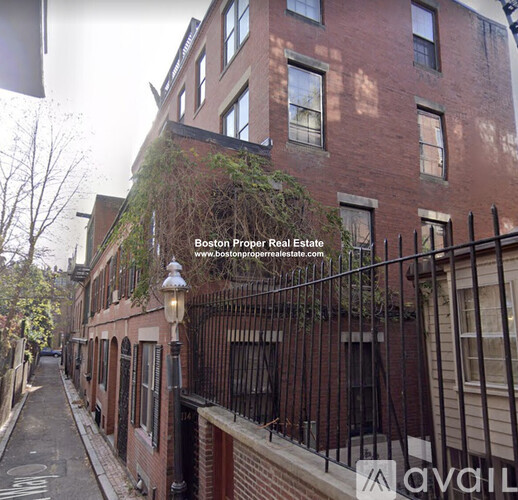 A narrow street with a red brick building on the right and a black iron fence.