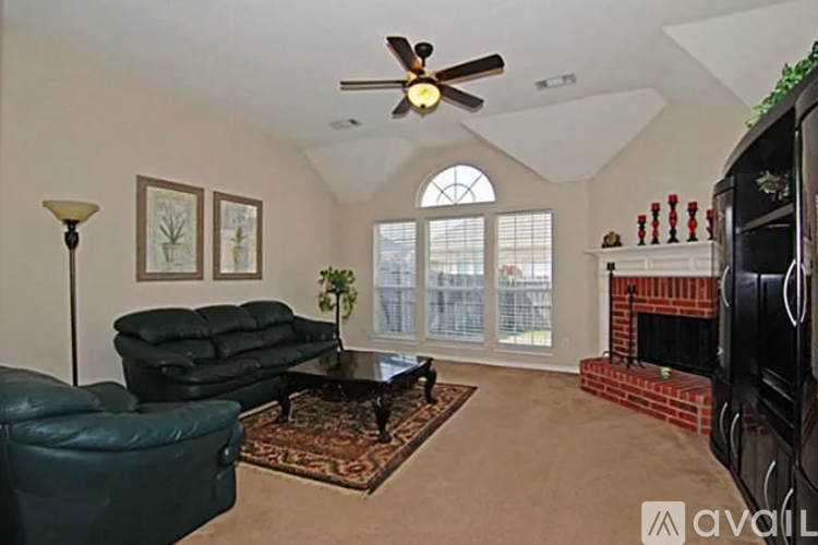 A living room with a black leather couch, a green leather chair, a coffee table, a fireplace, and a ceiling fan.
