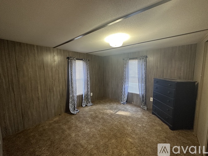 A bedroom with a carpeted floor, a window with curtains, and a dresser.