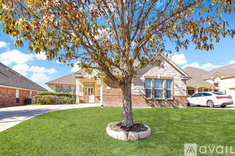 A tree with brown leaves is in front of a house with a car parked in the driveway.