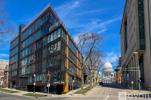 A modern building with a glass facade is situated on a street corner with a traffic light and a street sign.