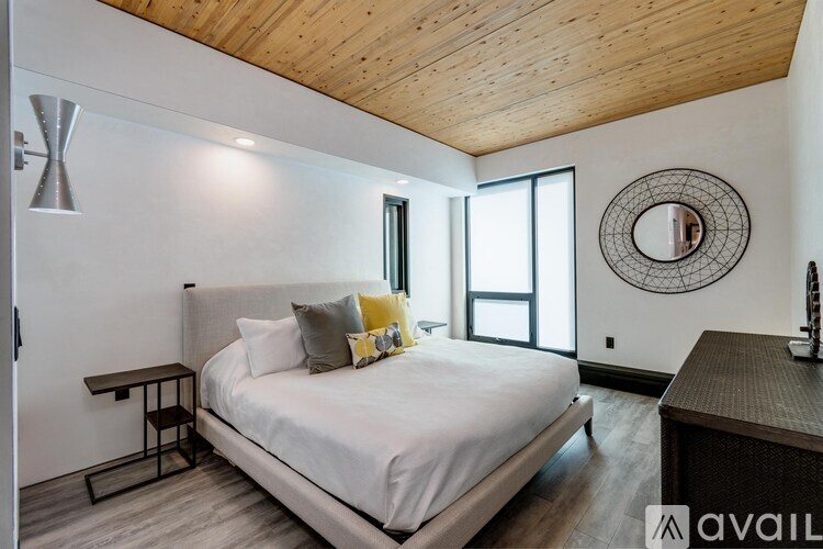 A bedroom with a large bed, a wooden ceiling, and a round mirror on the wall.