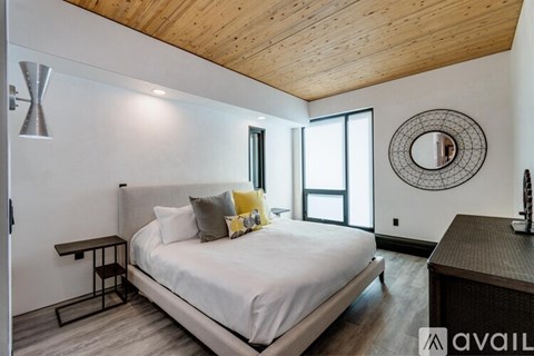 A bedroom with a large bed, a wooden ceiling, and a round mirror on the wall.
